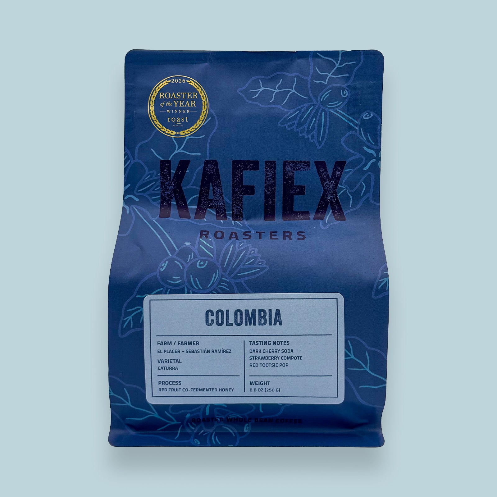 A blue bag of Kafiex Roasters Colombia coffee, featuring a gold Rooster of the Year 2023 award seal, on a light blue background.