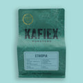 A stand-up pouch of KAFiEX ROASTERS Ethiopia coffee on a light aqua background. The pouch is dark green with white botanical line art, featuring a gold 'Roasted by Year 2023' seal and a white label with black text.